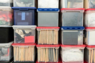 Stacked plastic file storage boxes with folders, binders and miscellaneous items.